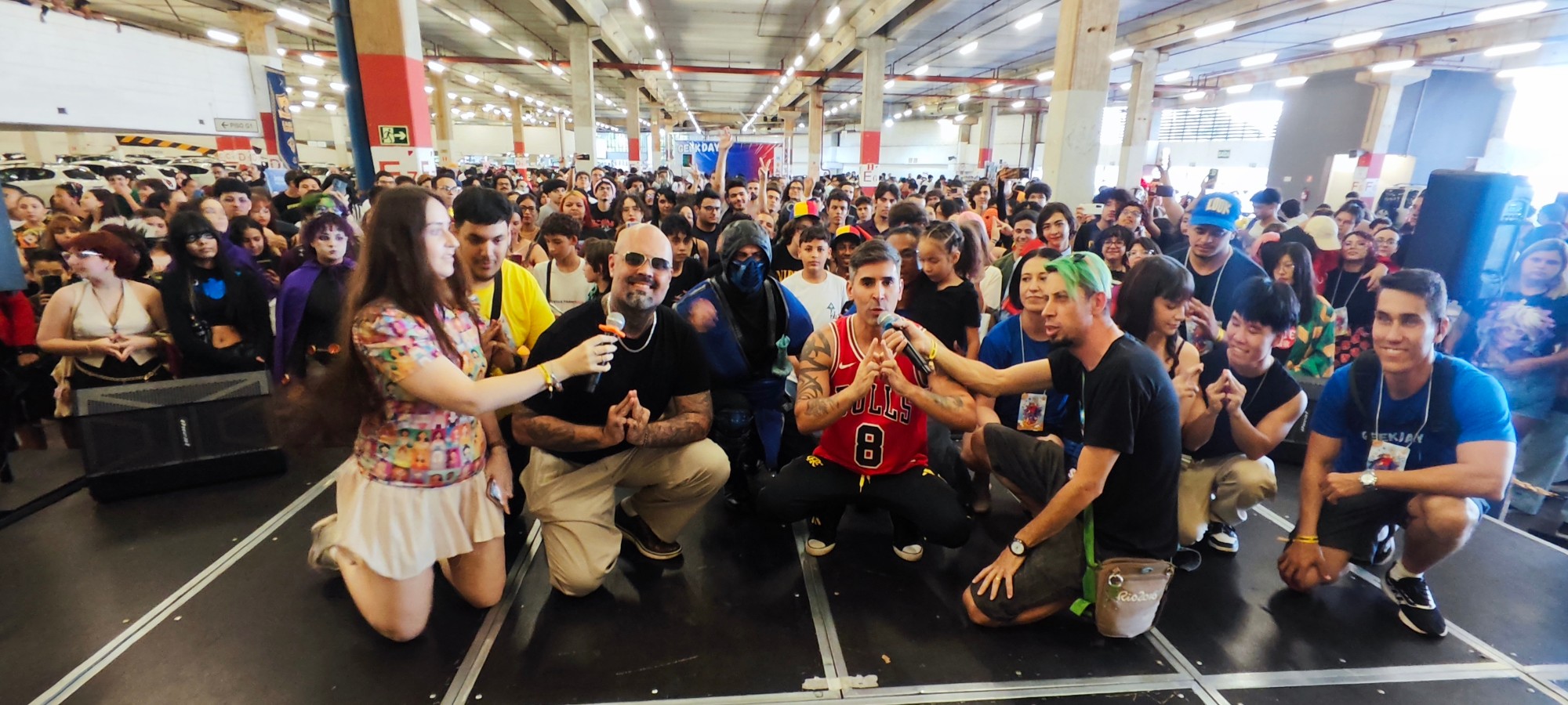 Convidados e cosplayers no palco com grande público ao fundo