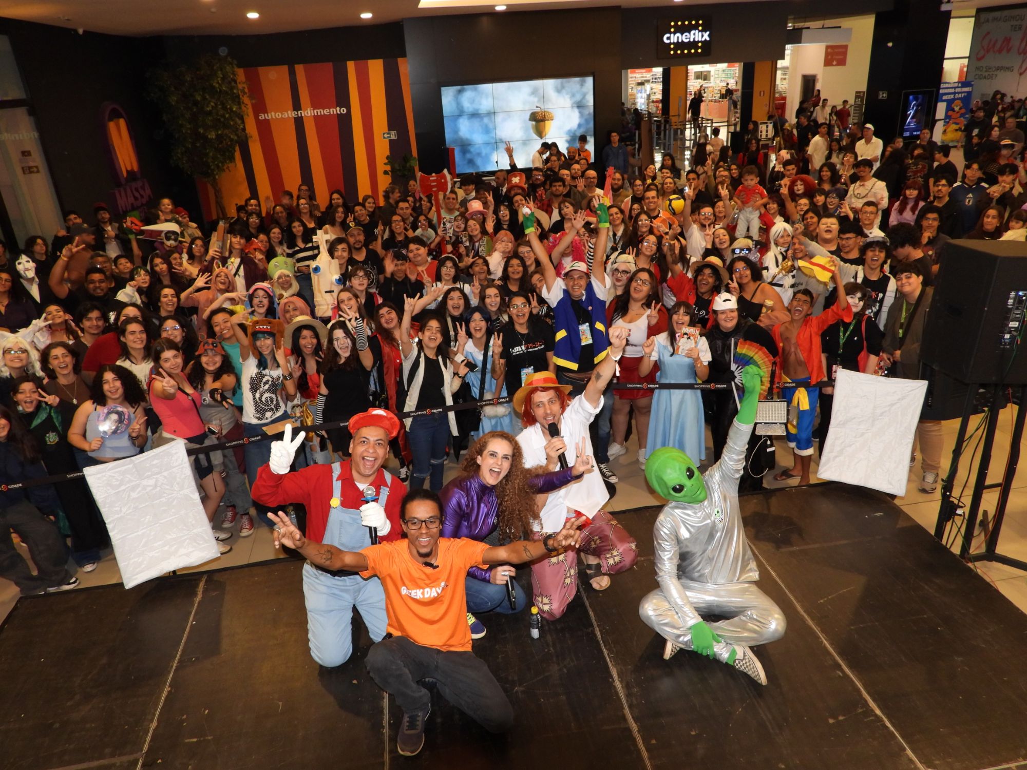 Apresentadores fantasiados e público celebrando no palco do Shopping Cidade